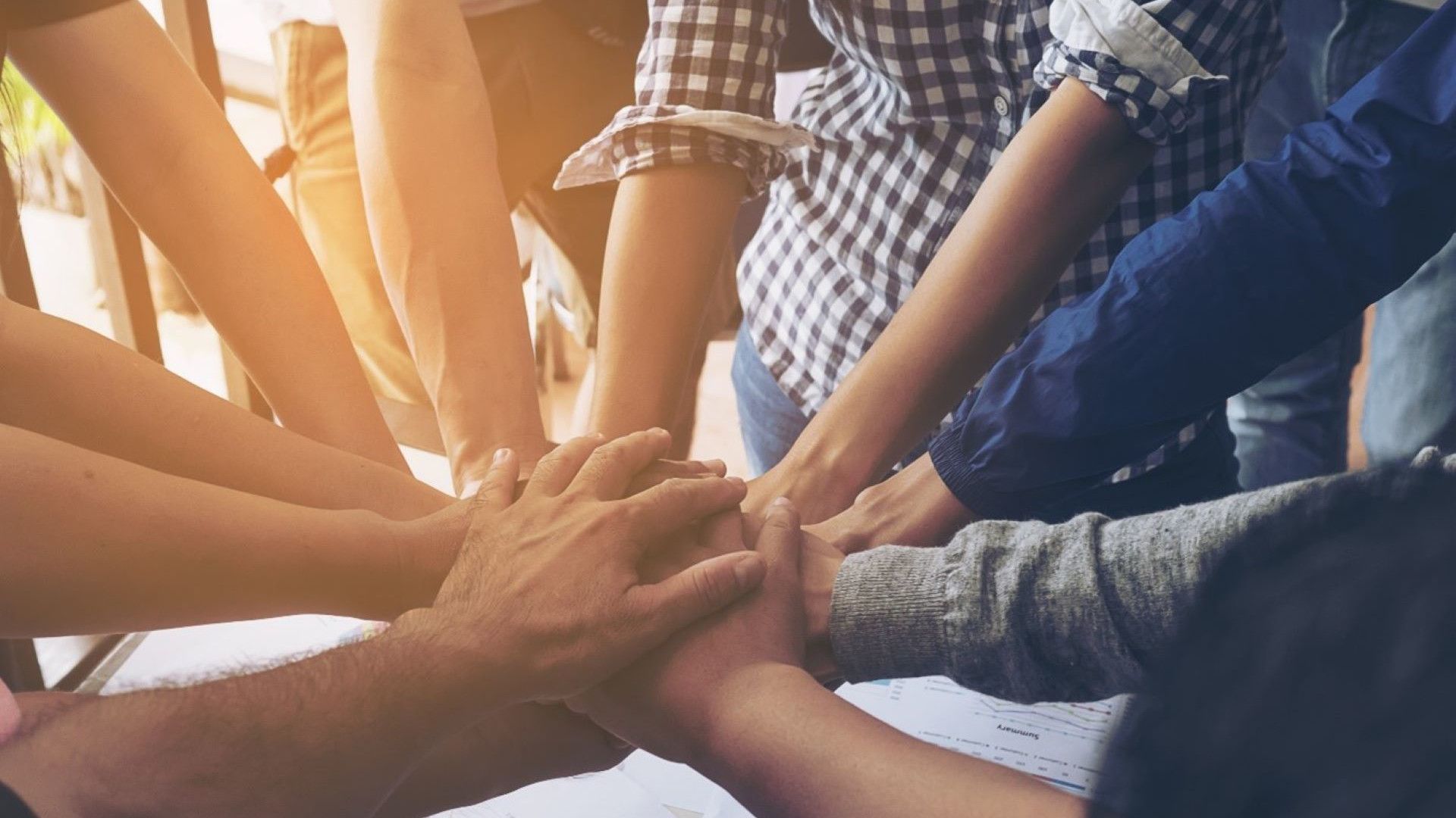 A group of people place their hands together in the center of a circle.