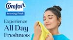 A woman smiling with her eyes closed, smelling a yellow shirt, next to the Comfort logo and the words 'Experience All Day Freshness'.