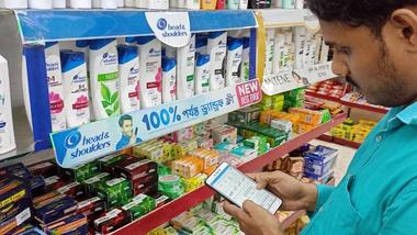 Man using a smartphone while browsing supermarket shelves stocked with personal care products.