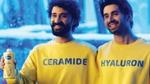 Two smiling men in yellow branded sweatshirts hold a Vaseline Deep Moisture lotion bottle against a blue background