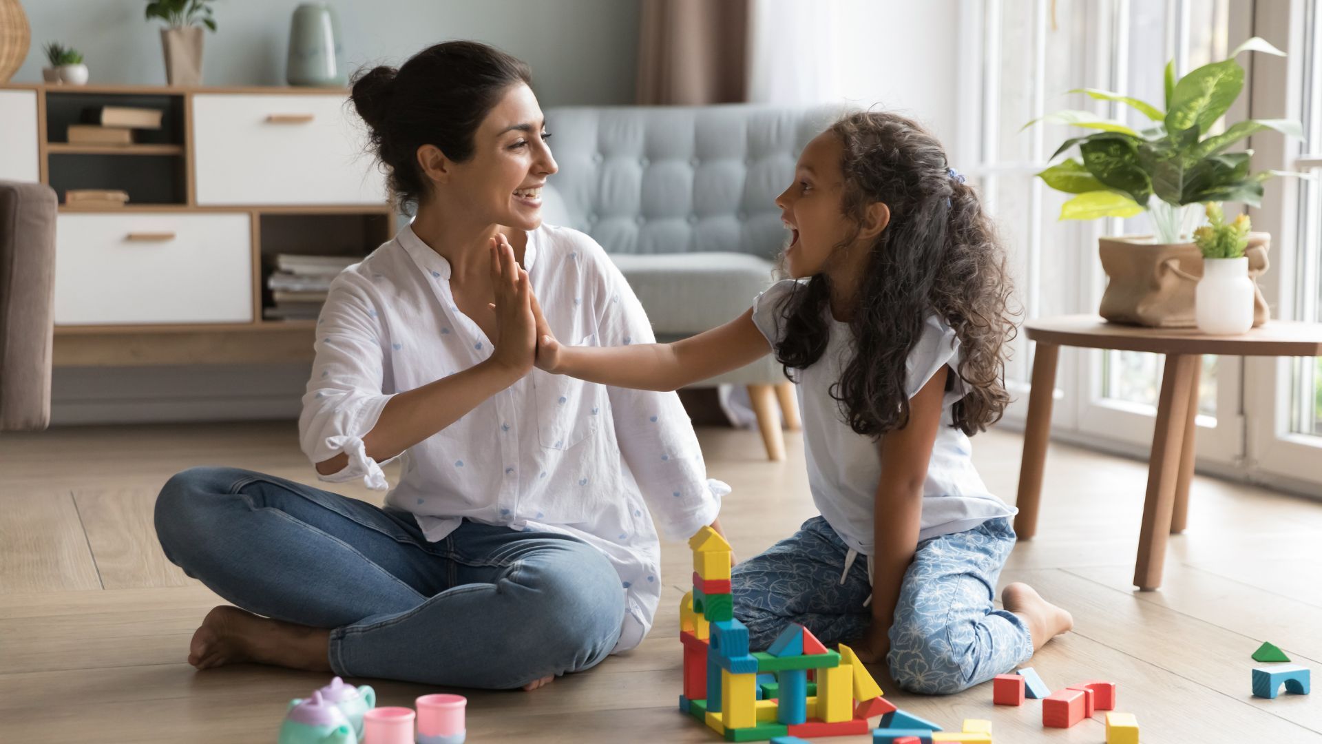 A mother and daughter playing with colourful building blocks on the floor.