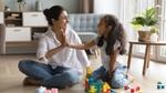 A mother and daughter playing with colourful building blocks on the floor.