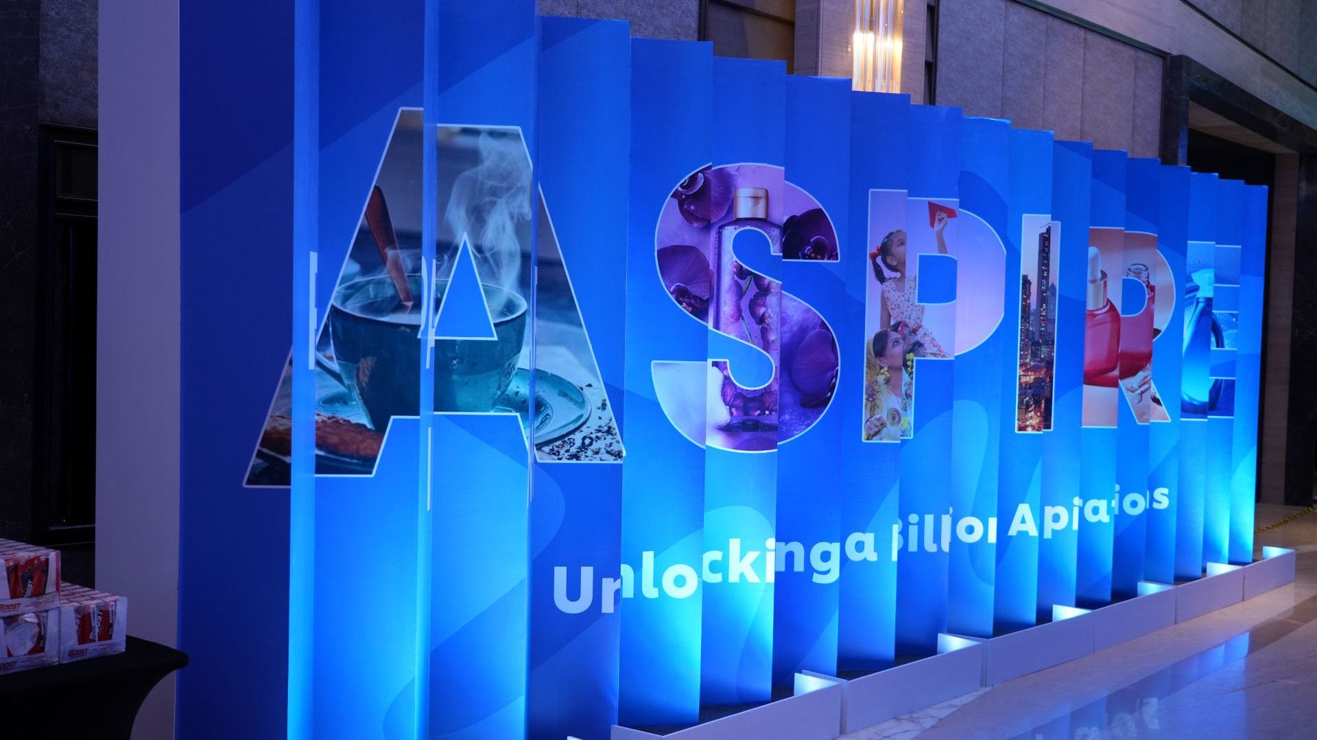A blue display with large letters spelling “ASPIRE,” partially showing the phrase “Unlocking a billion Aspirations,” is illuminated in a modern indoor setting.