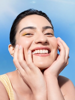 A person with a joyful expression, wearing a yellow outfit, smiles against a bright blue sky with a warm sunbeam.