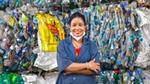 Smiling worker stands in front of a wall of compacted, recycled plastic bottles and packaging materials, promoting sustainable recycling practices.