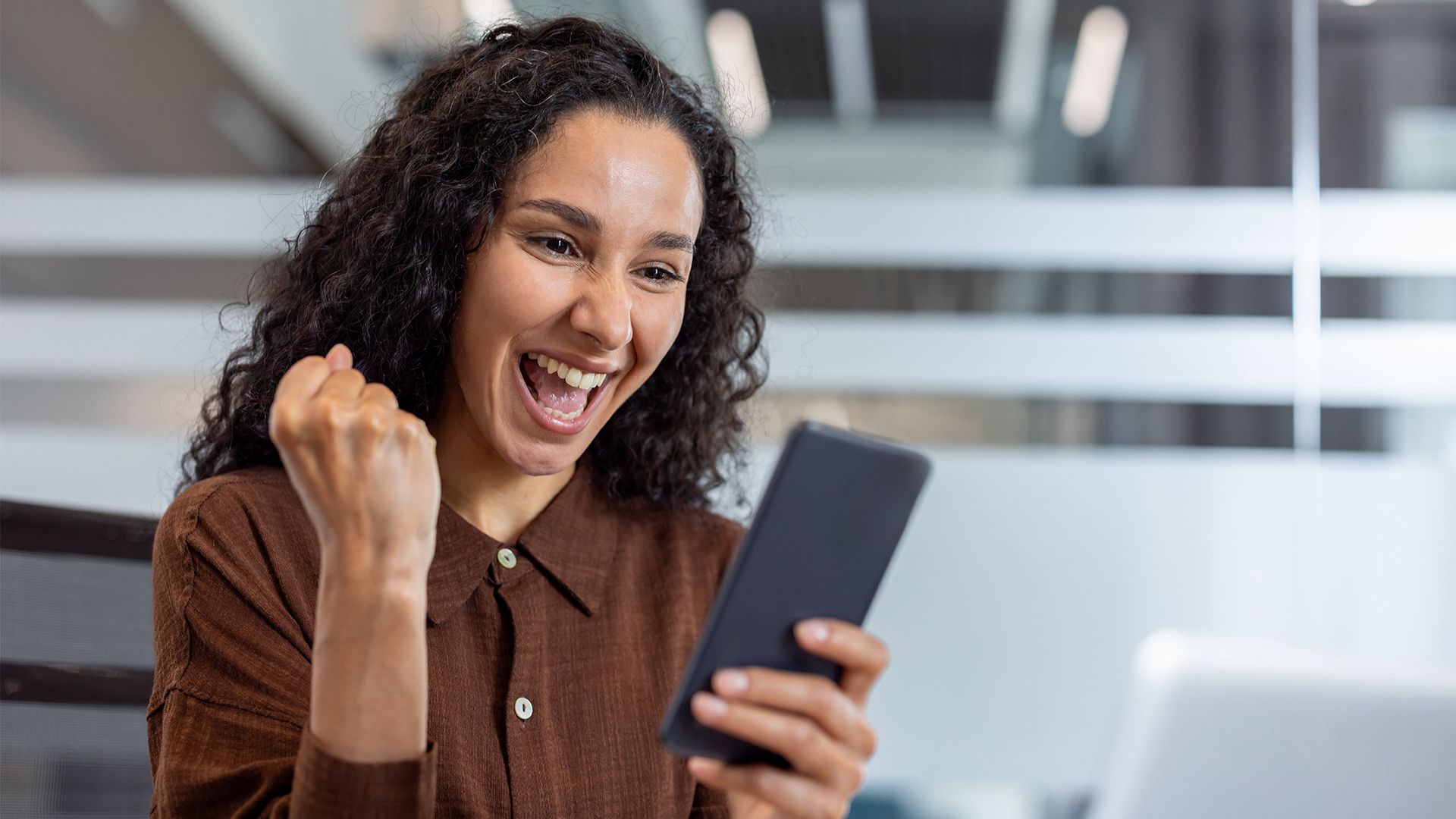 A woman cheering whilst looking at her mobile phone