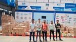 Five warehouse workers posing in front of stacked boxes.