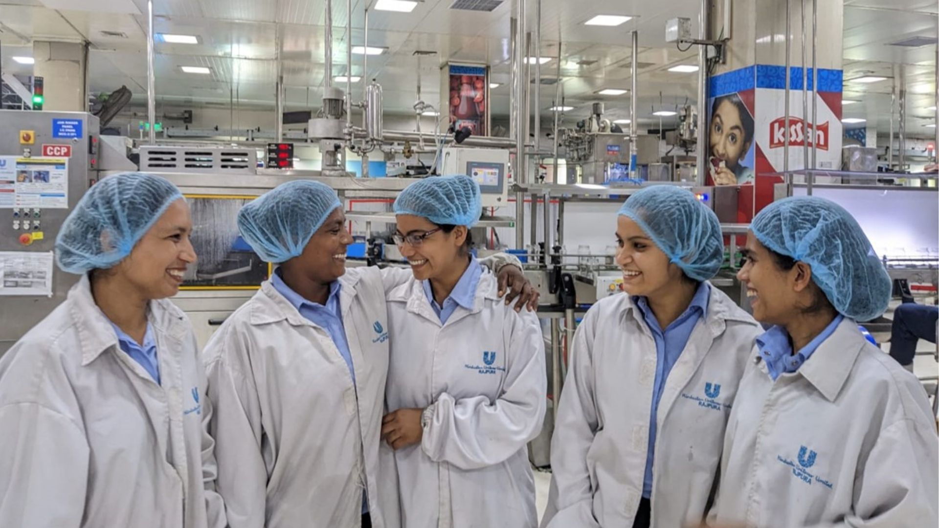 A group of women working at HUL's factory. They are wearing white coats and their hair is covered with a cap.