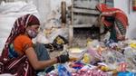 Two women wearing colourful saris and face masks, sorting through plastic waste.