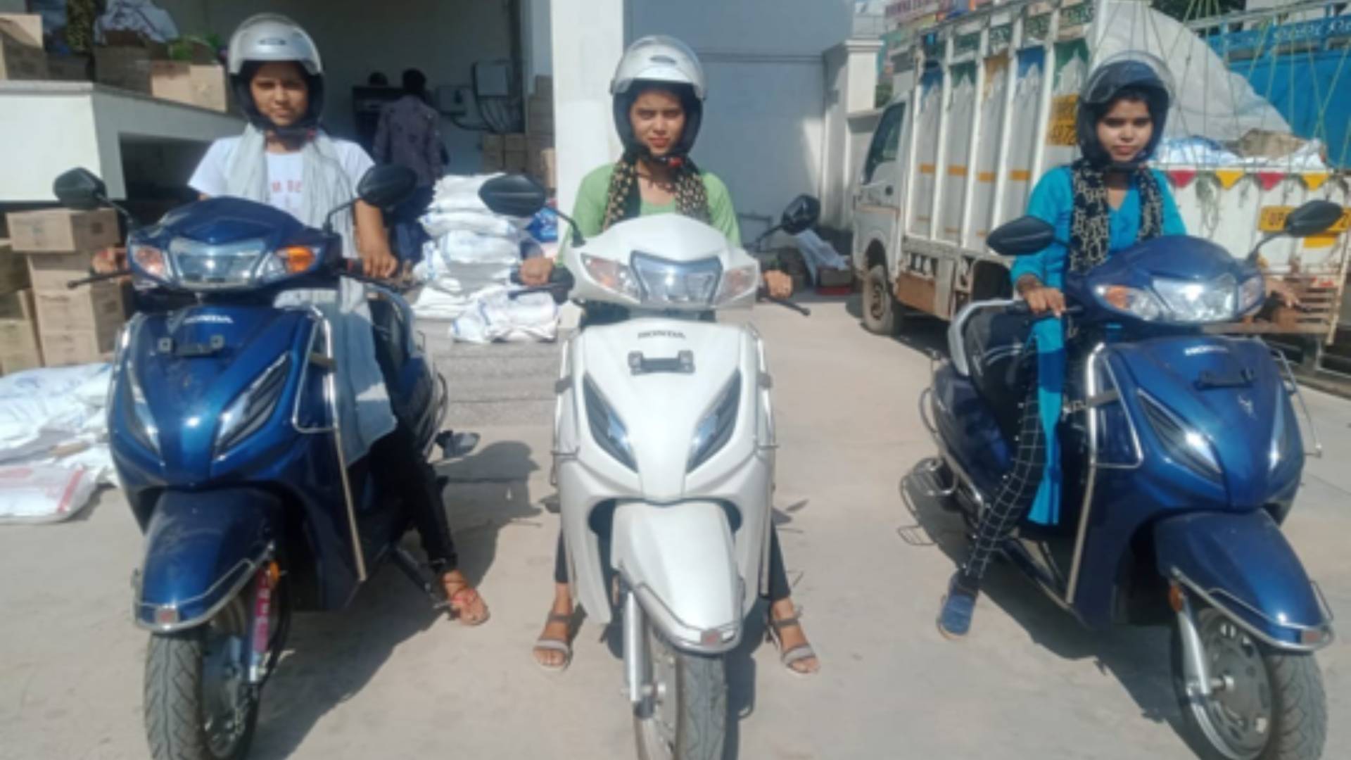 Three people on scooters wearing helmets in a driveway