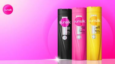 Three Sunsilk shampoo bottles in black, pink, and yellow, displayed against a vibrant pink gradient background with the Sunsilk logo in the top left corner.
