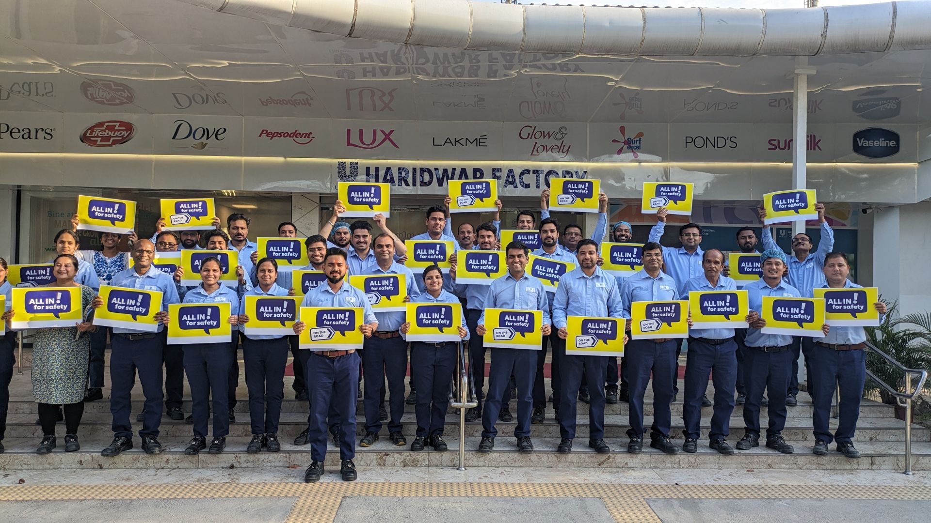 A group photo from HUL's factory site celebrating world safety week.  The employees are holding placards that read 'All in for Safety.'