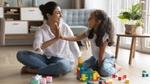 A woman and her daughter joyfully building a tower with colorful toy blocks on a play mat.
