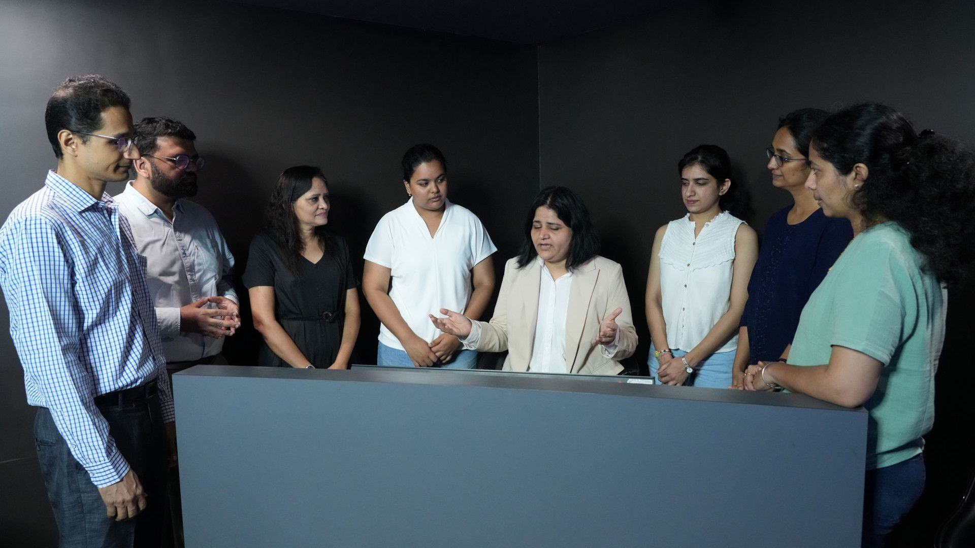Colleagues gather around a display as a woman leads a workplace discussion.