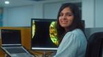 Young professional at a desk smiles toward the camera with data visualizations on her computer screen.