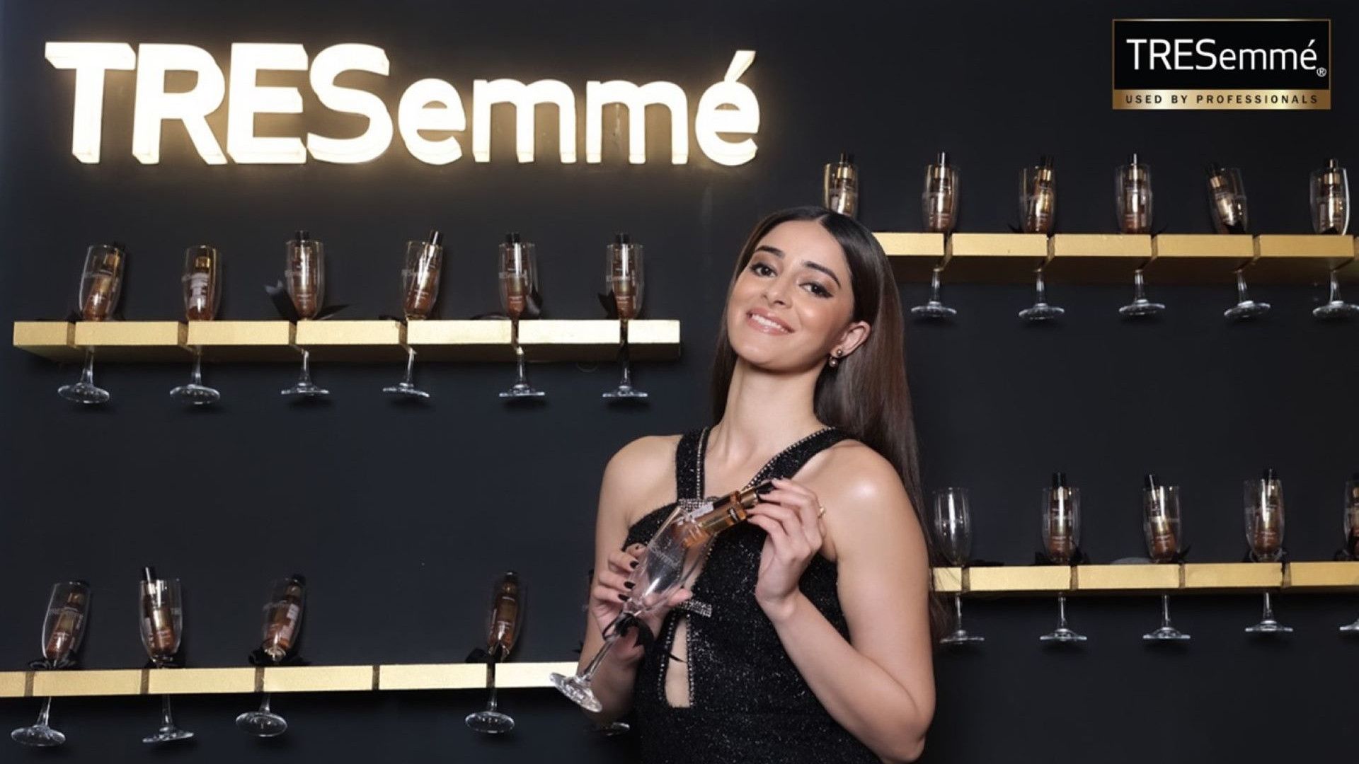 A woman in front of a wall of champagne glasses with TRESemmé products.