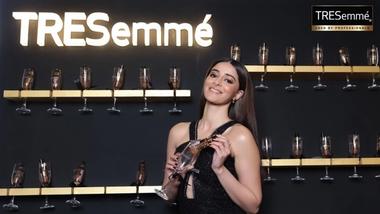 A woman in front of a wall of champagne glasses with TRESemmé products.