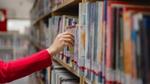 A woman reaching for a book from a full shelf in a library