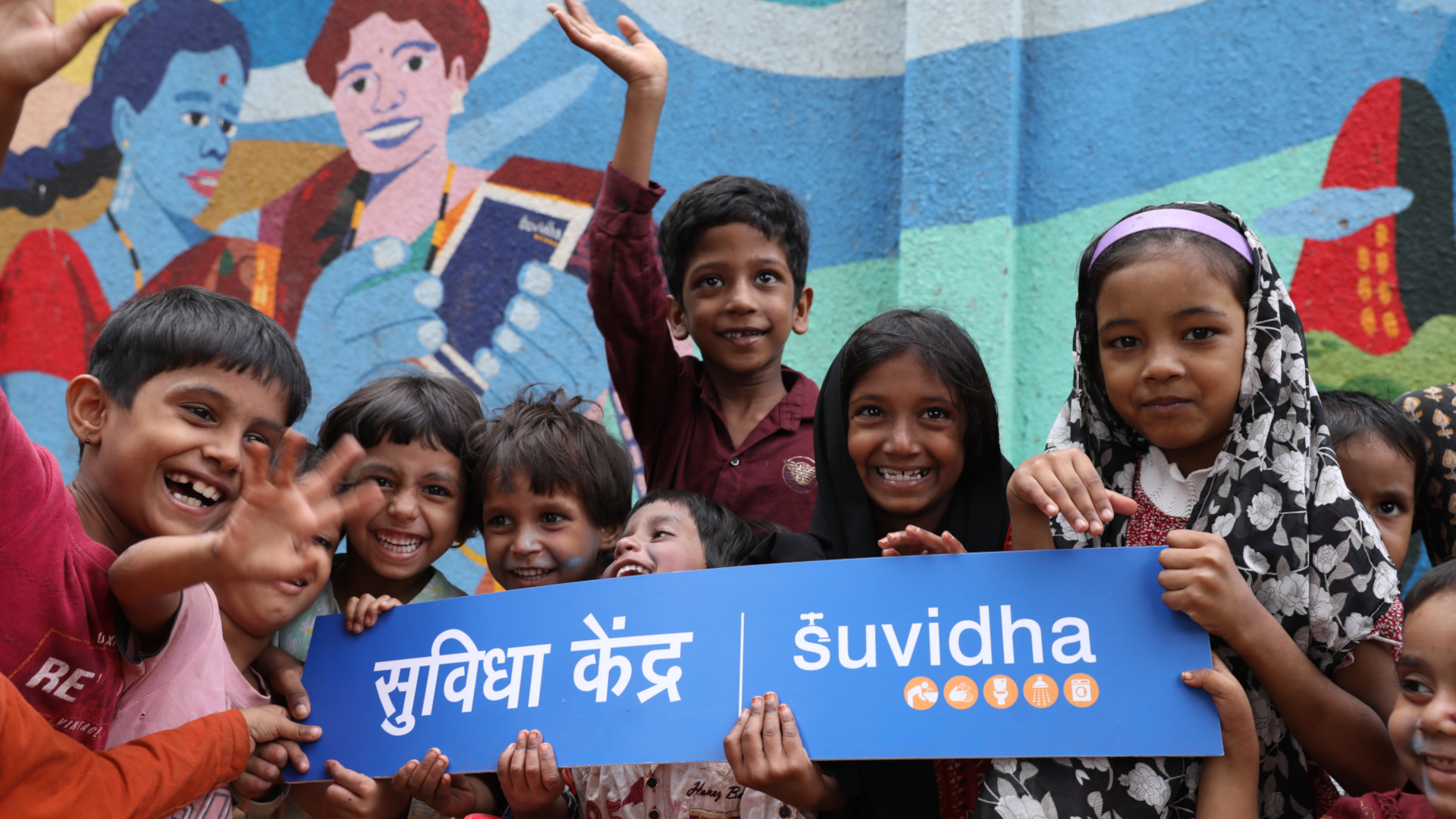 A group of smiling children sit in a row on steps outside a laundromat