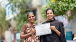 Two smiling women holding a certificate outdoors.