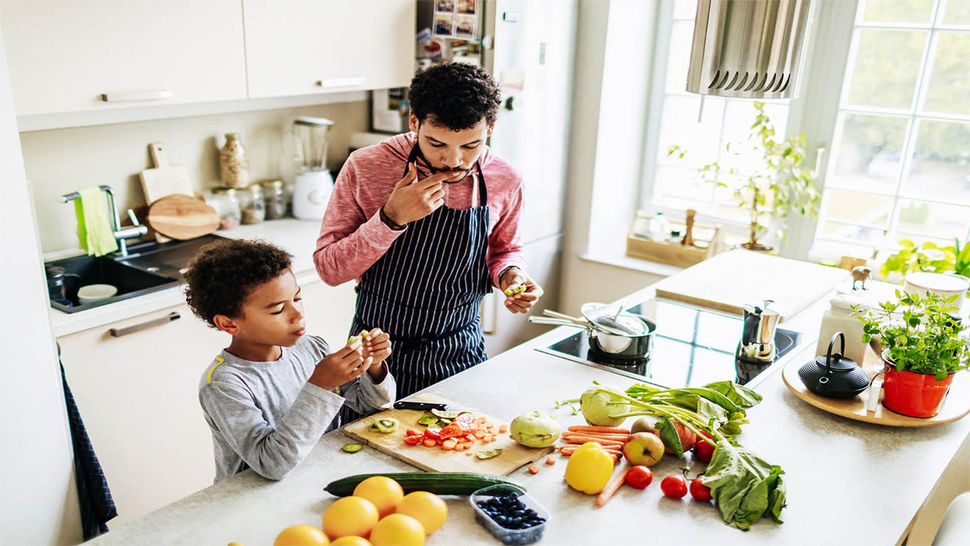 Man and young boy preparing, chopping and snacking on vegetables