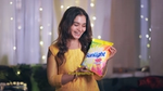 A smiling woman in a yellow outfit holds a colorful packet of Sunlight detergent, with fairy lights in the background.