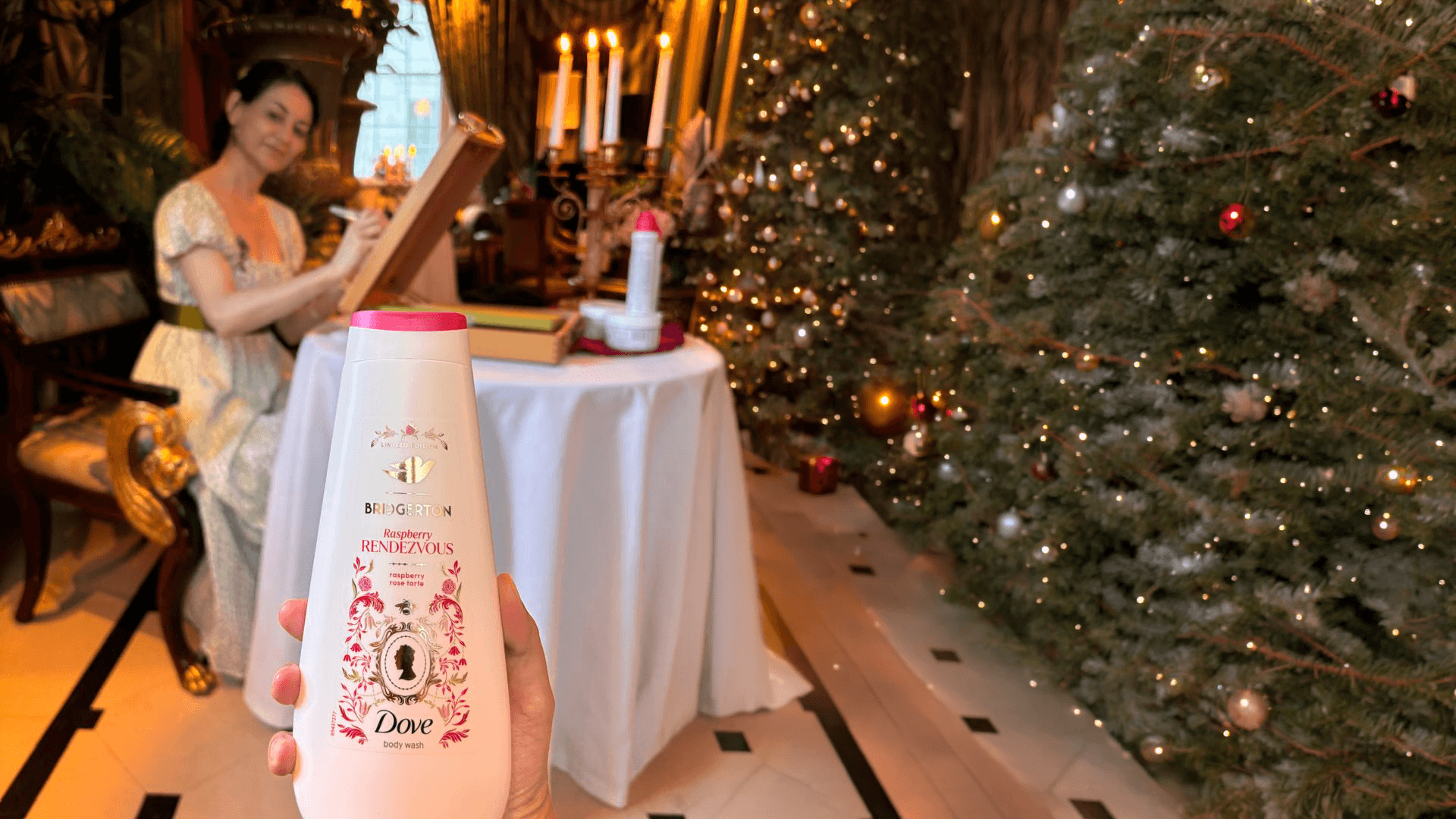 A festive scene with holiday decorations, a woman in the background painting at a table. In the foreground, a hand holds a bottle of Dove body wash.