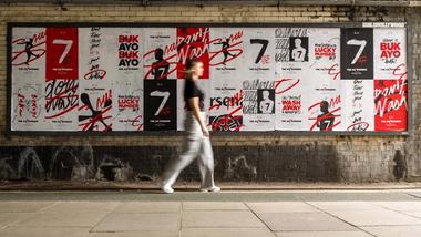 A woman walking past a brick wall covered in Persil Saka posters.