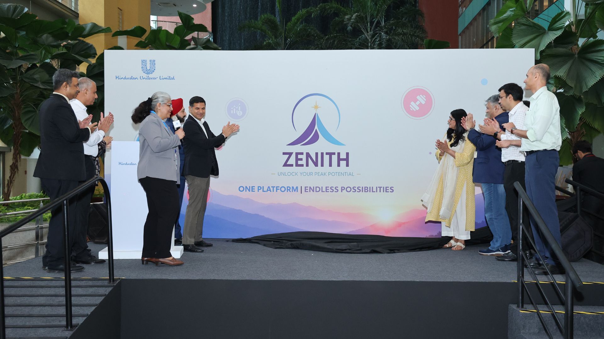 Employees stand on stage applauding the unveiling of the Zenith corporate platform banner