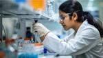 A woman in a lab coat carefully examines a test tube in a laboratory setting.