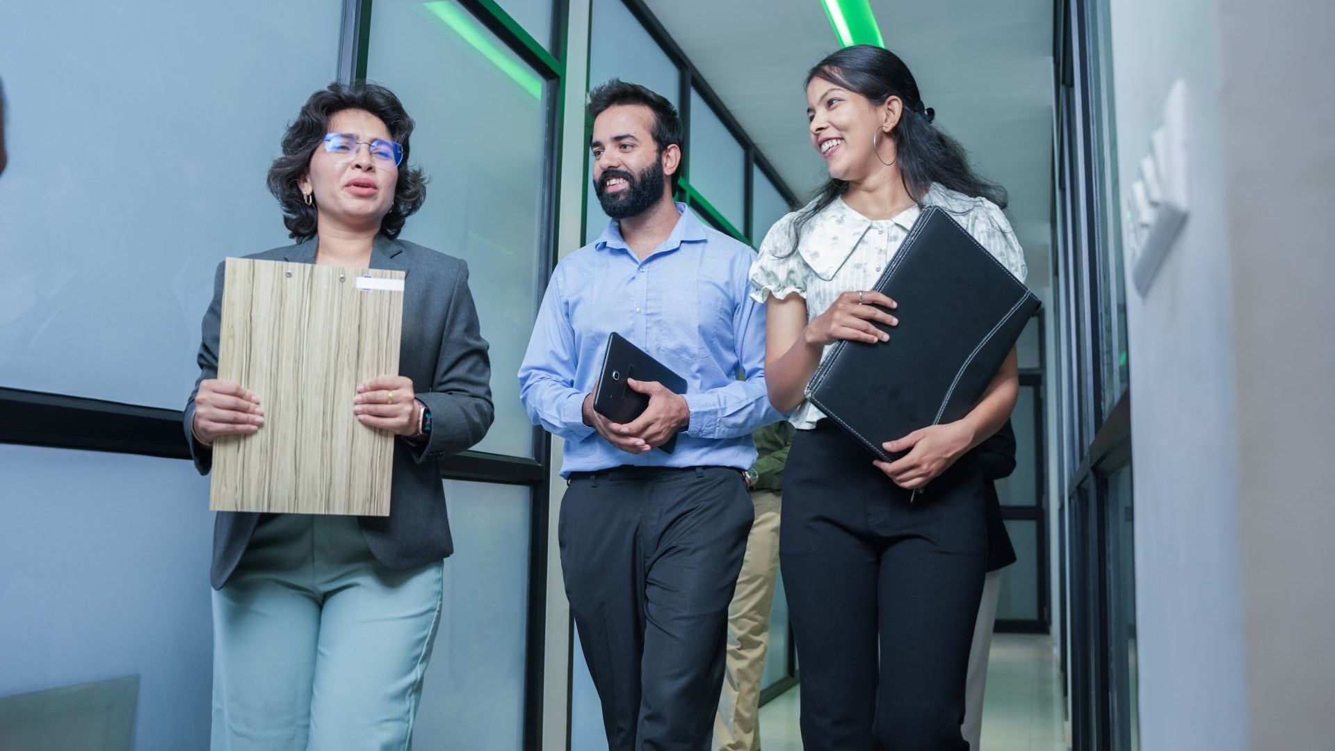 Three employees walking down an aisle in a corporate setting.
