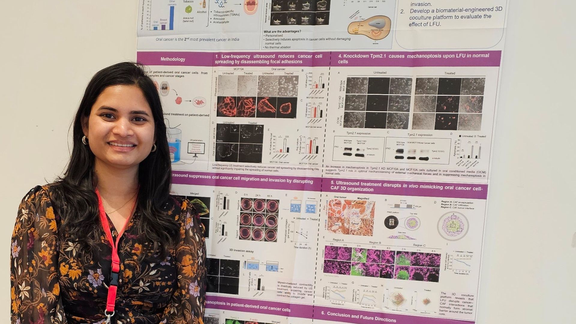 Researcher standing and smiling in front of a detailed scientific poster on oral cancer studies.