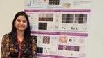 Researcher standing and smiling in front of a detailed scientific poster on oral cancer studies.
