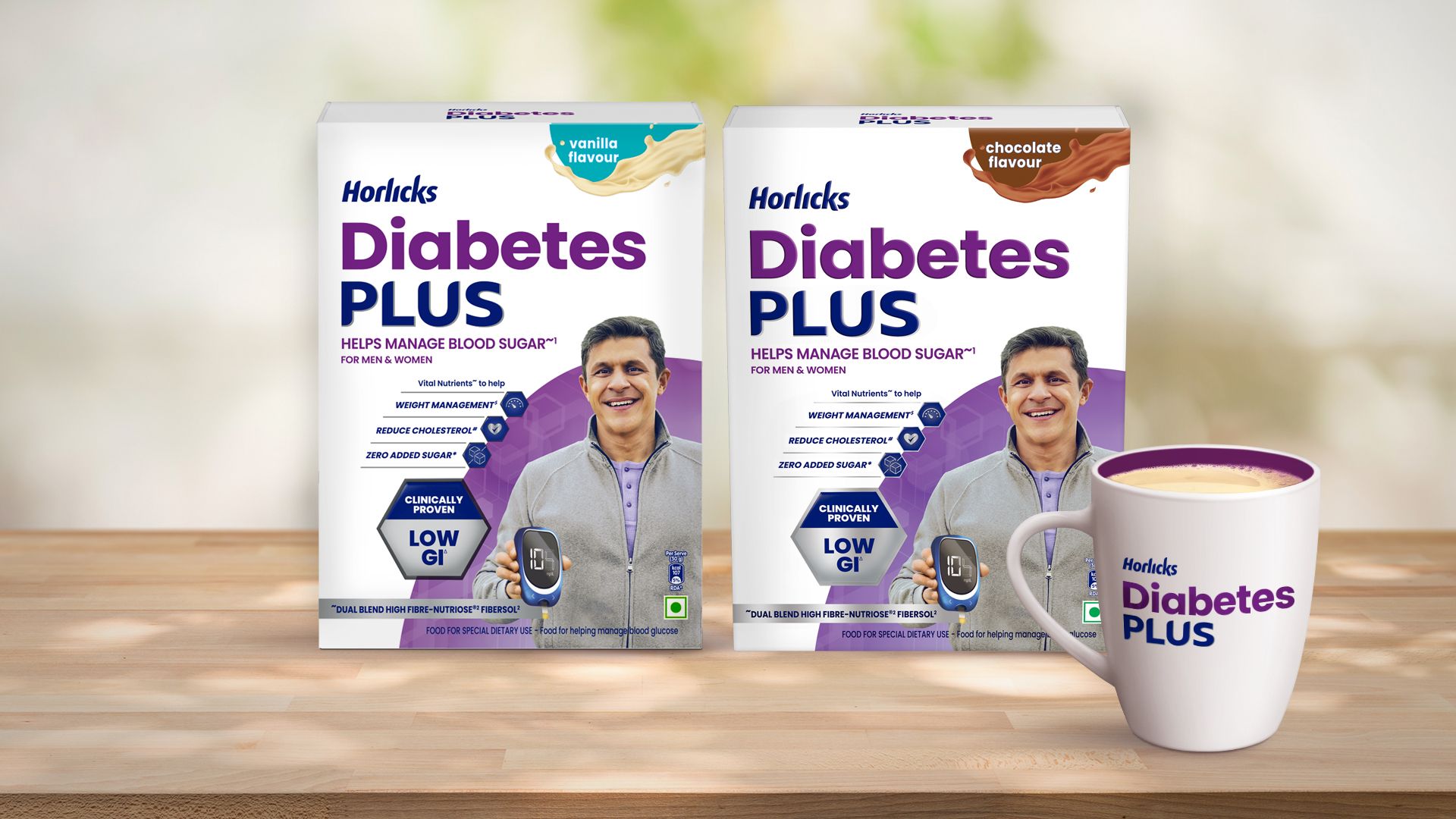 Two packs of Horlicks Diabetes Plus in vanilla and chocolate flavours featuring a smiling older man, along with a Diabetes Plus branded mug displayed on a wooden surface.