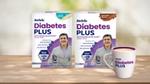 Two packs of Horlicks Diabetes Plus in vanilla and chocolate flavours featuring a smiling older man, along with a Diabetes Plus branded mug displayed on a wooden surface.