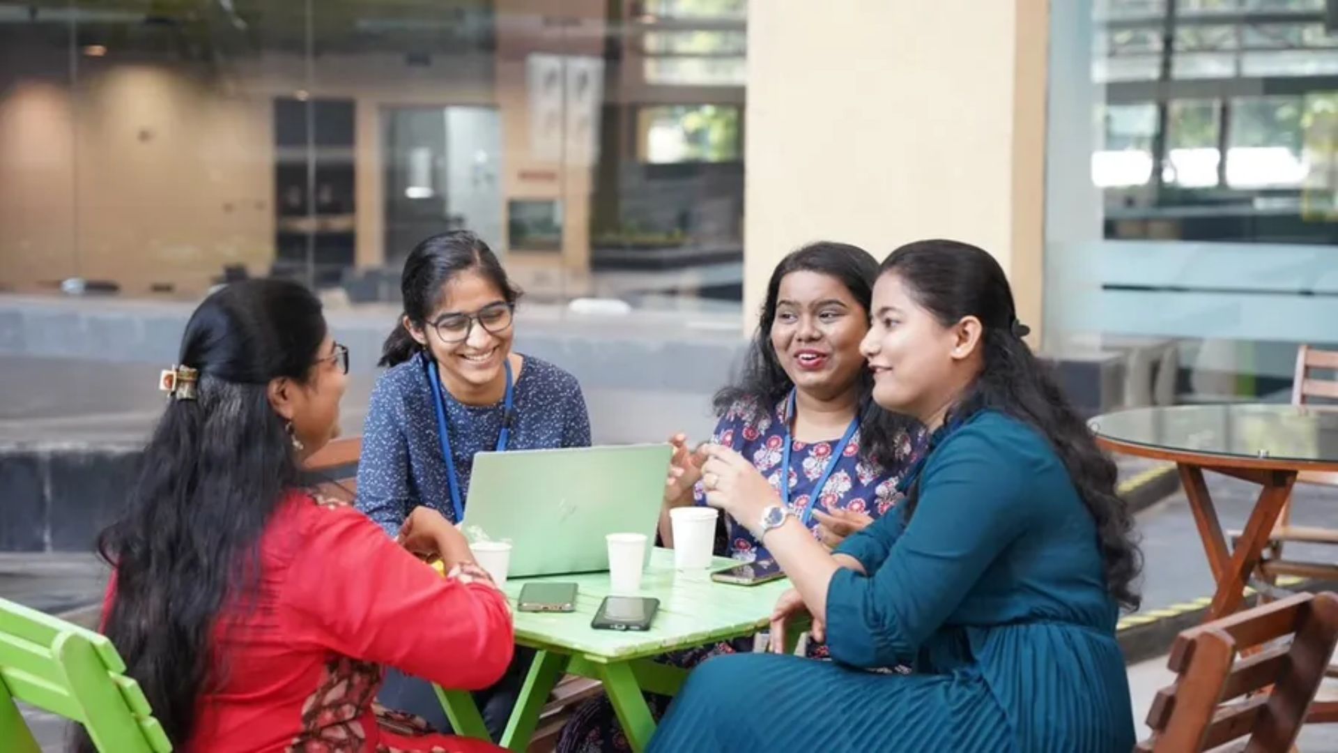 A group of women chatting at a table with a computer and cups