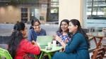 A group of women chatting at a table with a computer and cups