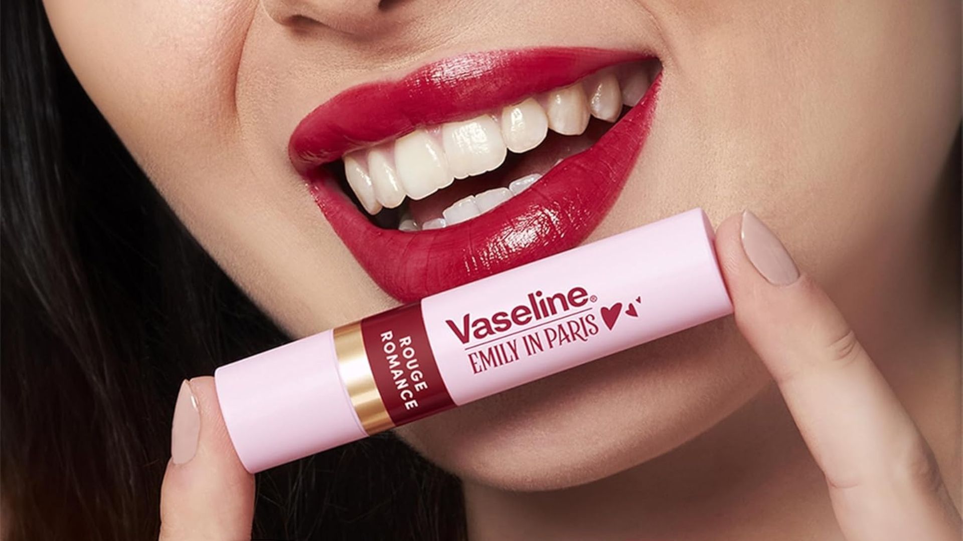 Smiling woman with red lips holding a Vaseline Emily in Paris Rouge Romance moisturizing lip balm