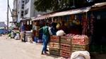 A woman shops at a market in rural India. Fruit is hanging overhead. Boxes full of vegetables.