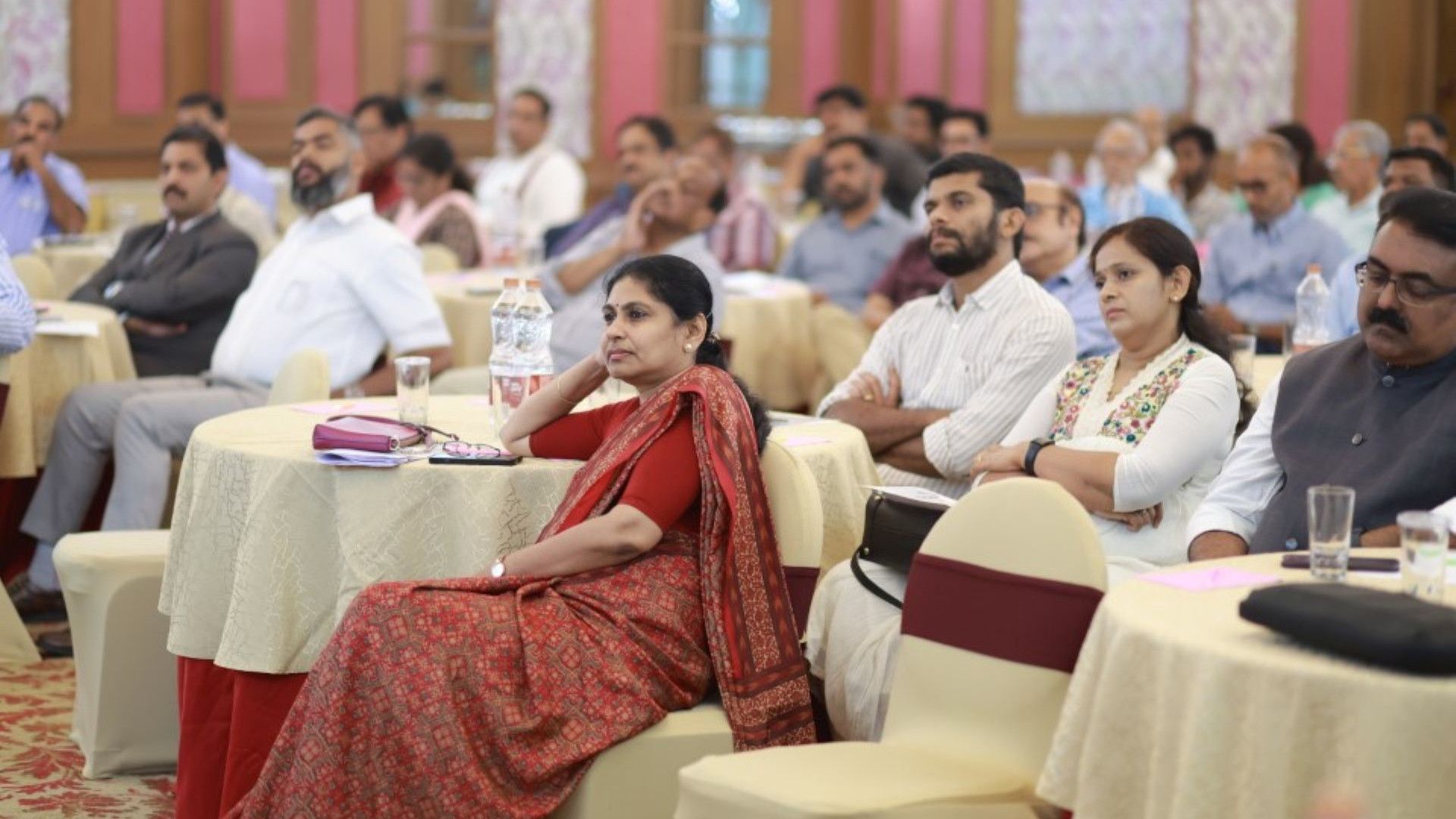 A group of attentive participants seated at tables during a seminar in a spacious, well-decorated room.
