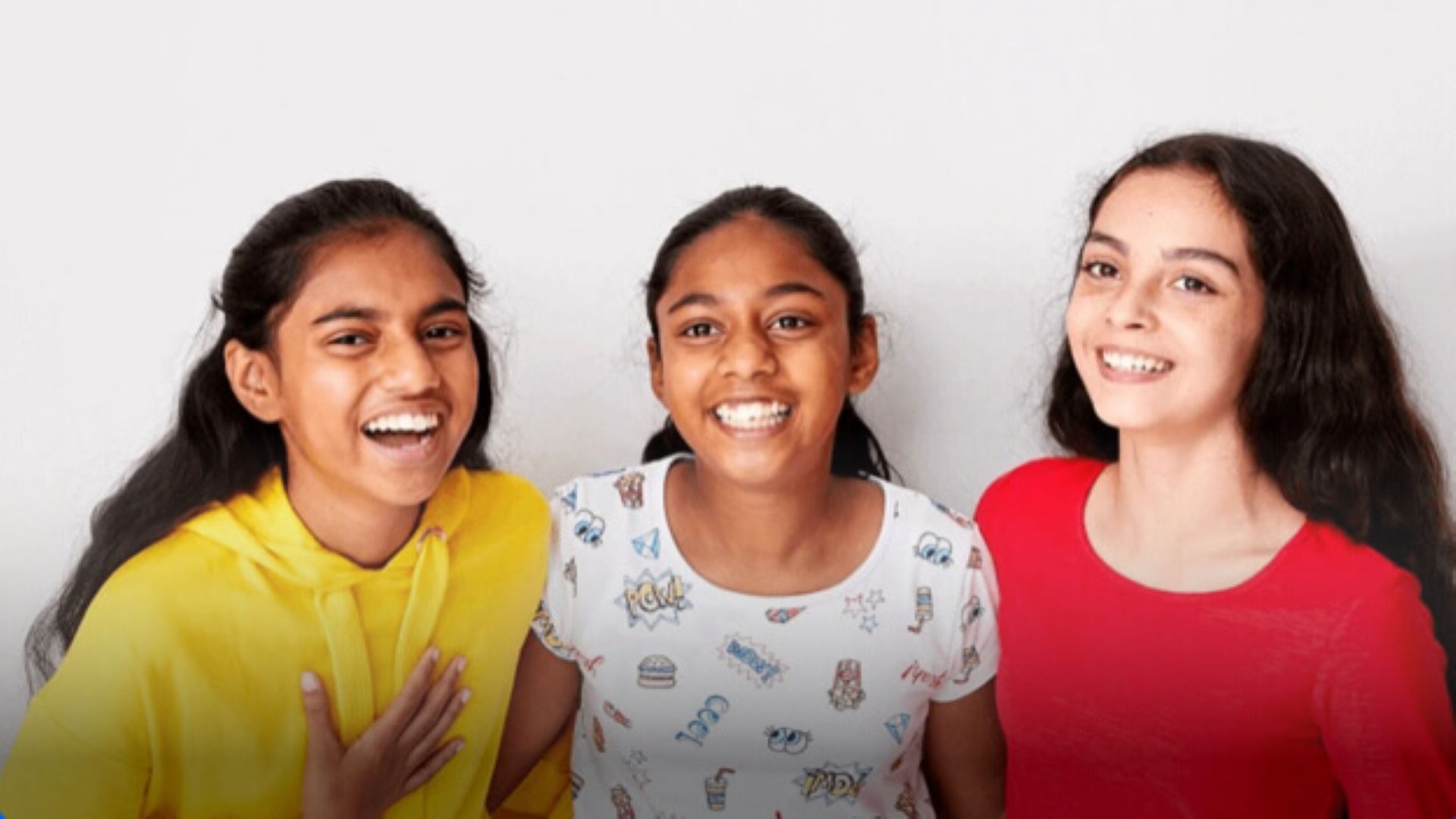 An image of three young girls standing together and laughing. 