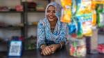 Smiling woman in floral attire at a small shop counter.