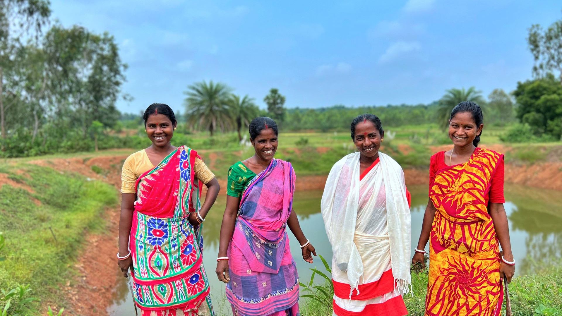 Four women in saris standing in the countryside.