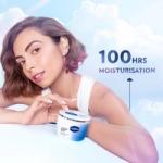 Woman posing with a Vaseline Cloud Soft moisturiser tub against a soft cloudy background and 100 hours claim text