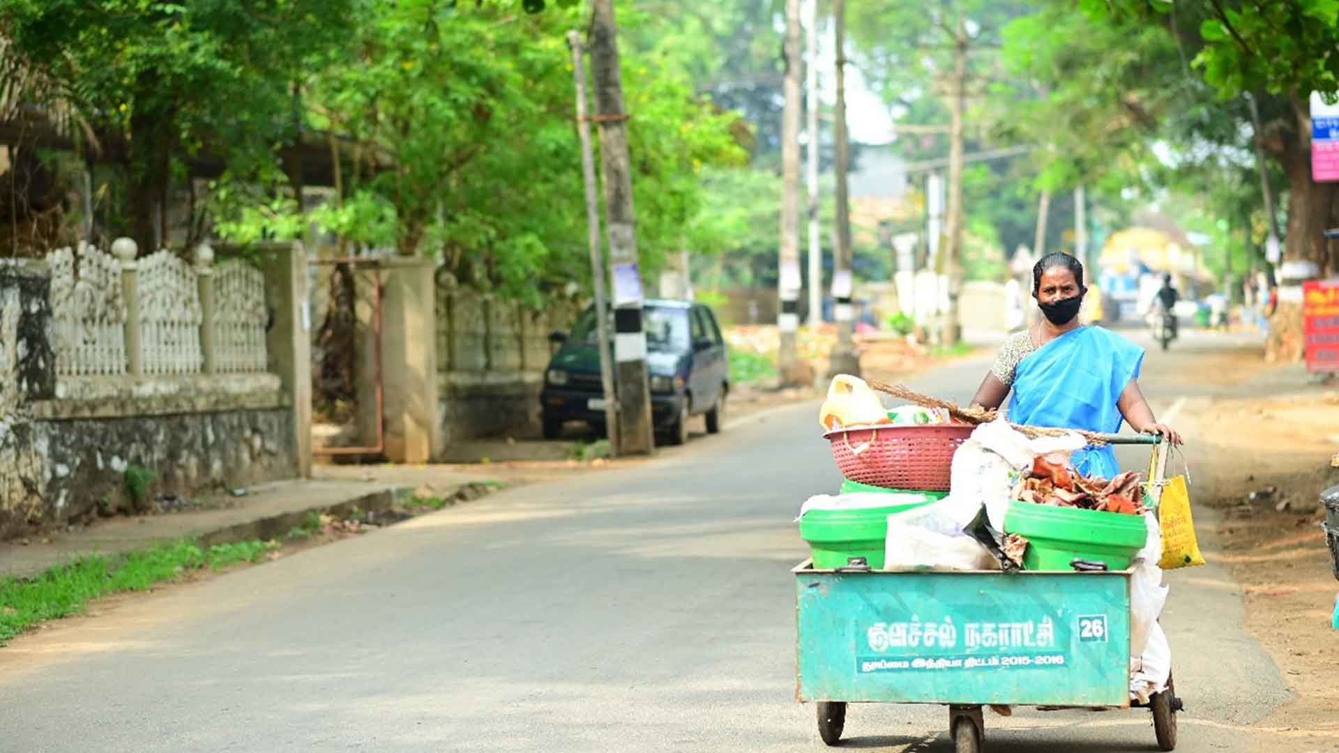 An image of a handcart with segregated dry waste. A lady wearing a blue sari is pushing the cart.